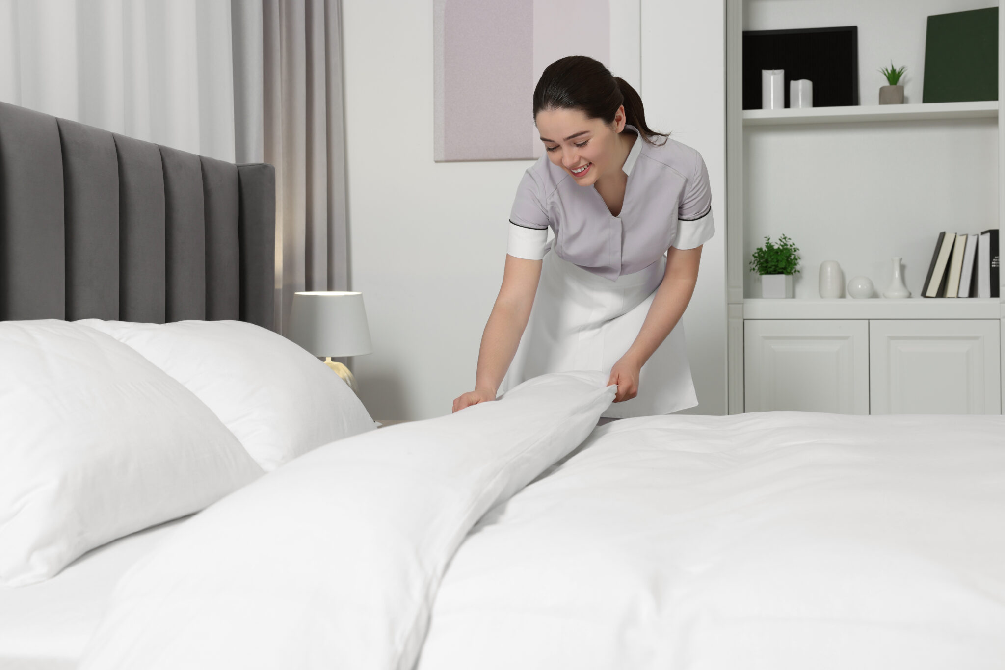 A cleaner making a bed with crisp white linens during a vacation-rental clean