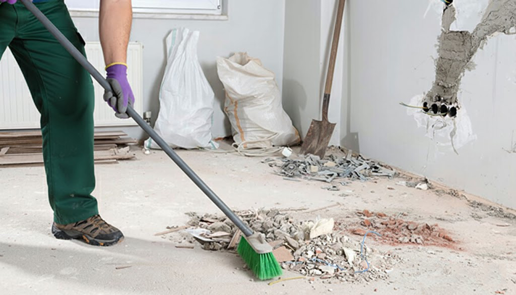 A worker sweeping up construction debris and dust in a room being renovated